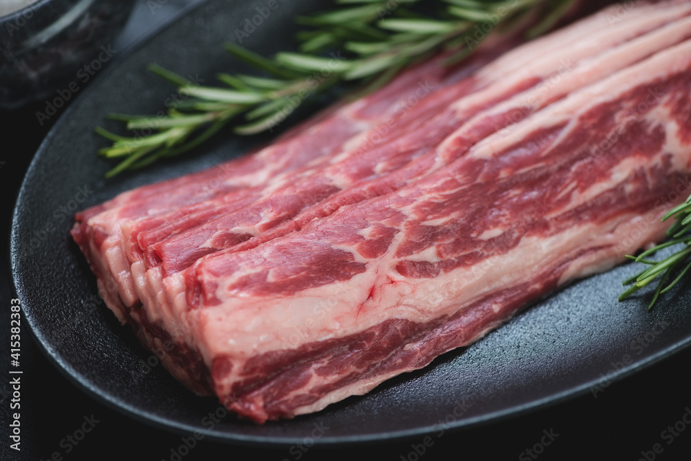 Close-up of raw fresh bacon made of marbled beef on a black plate, selective focus, studio shot