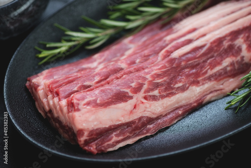 Close-up of raw fresh bacon made of marbled beef on a black plate, selective focus, studio shot