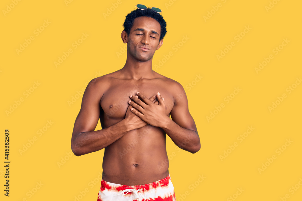 Fototapeta premium African handsome man wearing swimsuit and sunglasses smiling with hands on chest with closed eyes and grateful gesture on face. health concept.