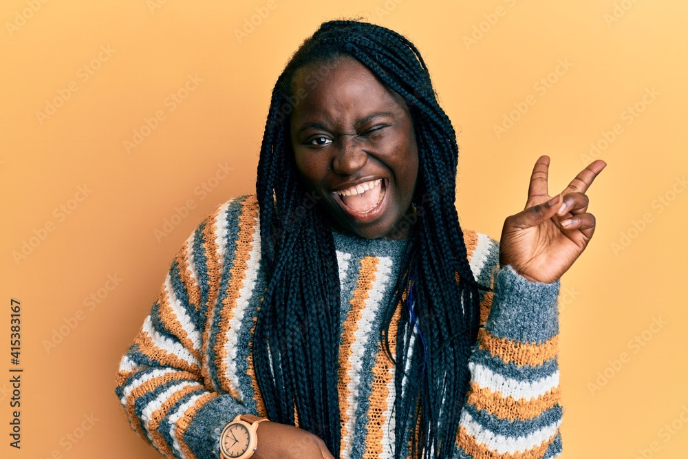 Young black woman with braids wearing casual winter sweater smiling with happy face winking at the camera doing victory sign with fingers. number two. Young black woman with braids wearing casual winter sweater smiling with happy face winking at the camera doing victory sign with fingers. number two.