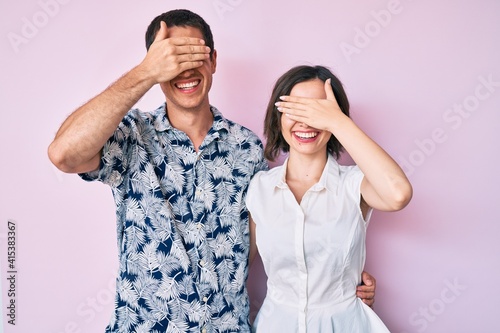 Beautiful couple wearing casual clothes smiling and laughing with hand on face covering eyes for surprise. blind concept.