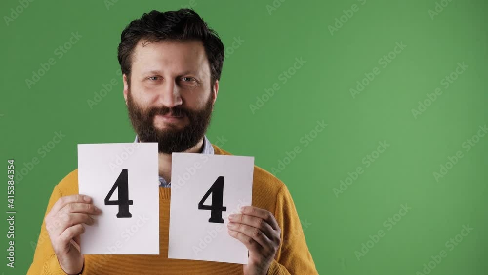 Man holding number 44 sign. Cheerful white bearded good-looking man in yellow sweater shows number forty-four on white sheet. Chrome key, green screen, copy space Man holding number 44 sign. Cheerful white bearded good-looking man in yellow sweater shows number forty-four on white sheet. Chrome key, green screen, copy space