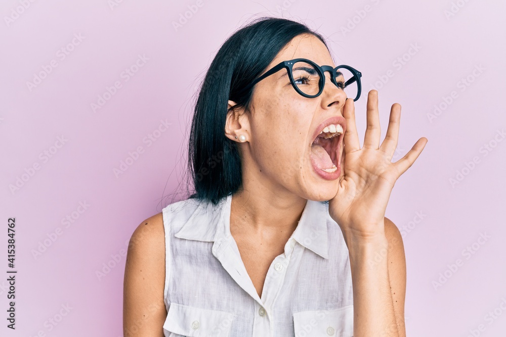Beautiful young woman holding pink cancer ribbon clueless and confused expression with arms and hands raised. doubt concept. Beautiful young woman holding pink cancer ribbon clueless and confused expression with arms and hands raised. doubt concept.