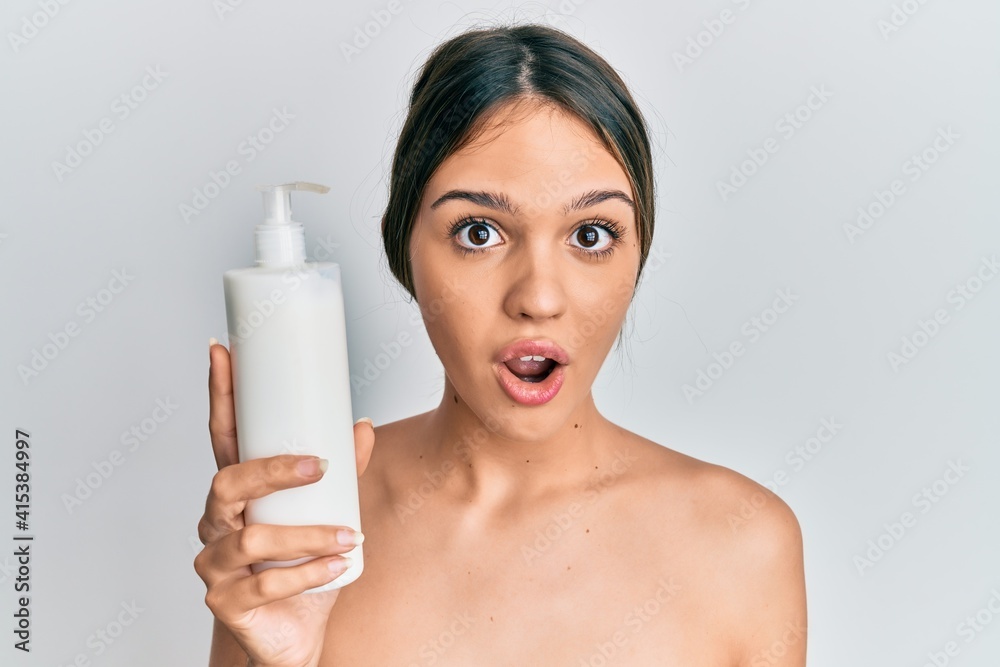 Young brunette woman holding cosmetic moisturizer facial cream scared and amazed with open mouth for surprise, disbelief face Young brunette woman holding cosmetic moisturizer facial cream scared and amazed with open mouth for surprise, disbelief face