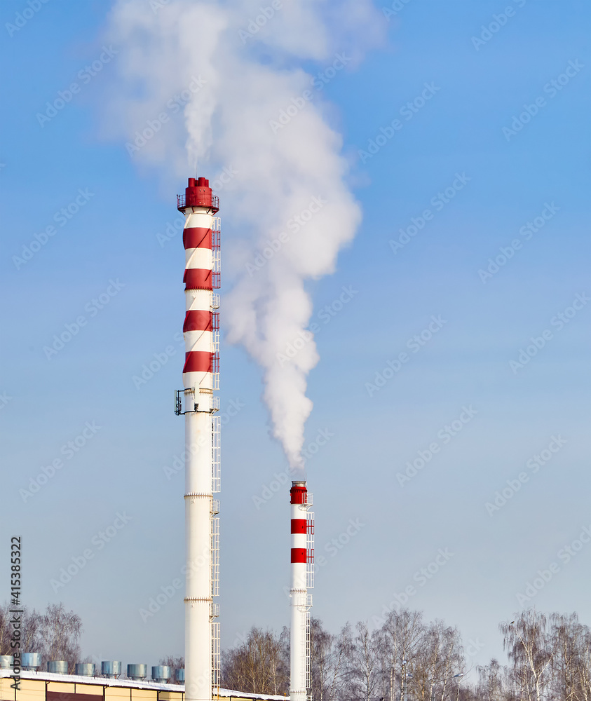 Steam from pipes to heat a building against a blue sky.City landscape.Vertical photo. Steam from pipes to heat a building against a blue sky.City landscape.Vertical photo.