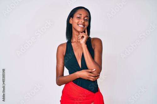 Young african american woman wearing swimsuit looking confident at the camera with smile with crossed arms and hand raised on chin. thinking positive.
