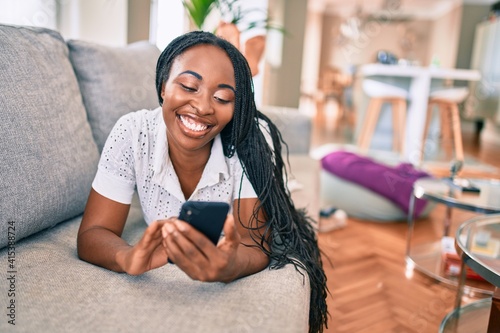 Young african american woman smiling happy using smartphone laying on the sofa at home