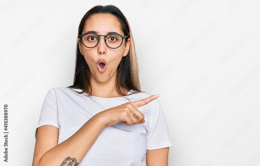 Young hispanic woman wearing casual white t shirt surprised pointing with finger to the side, open mouth amazed expression. Young hispanic woman wearing casual white t shirt surprised pointing with finger to the side, open mouth amazed expression.