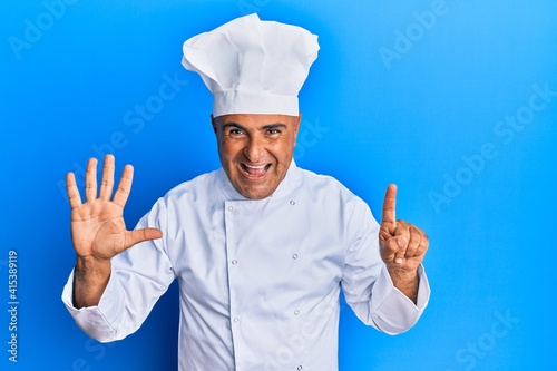 Mature middle east man wearing professional cook uniform and hat showing and pointing up with fingers number six while smiling confident and happy.