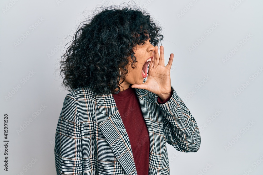Young hispanic woman wearing business clothes shouting and screaming loud to side with hand on mouth. communication concept. Young hispanic woman wearing business clothes shouting and screaming loud to side with hand on mouth. communication concept.