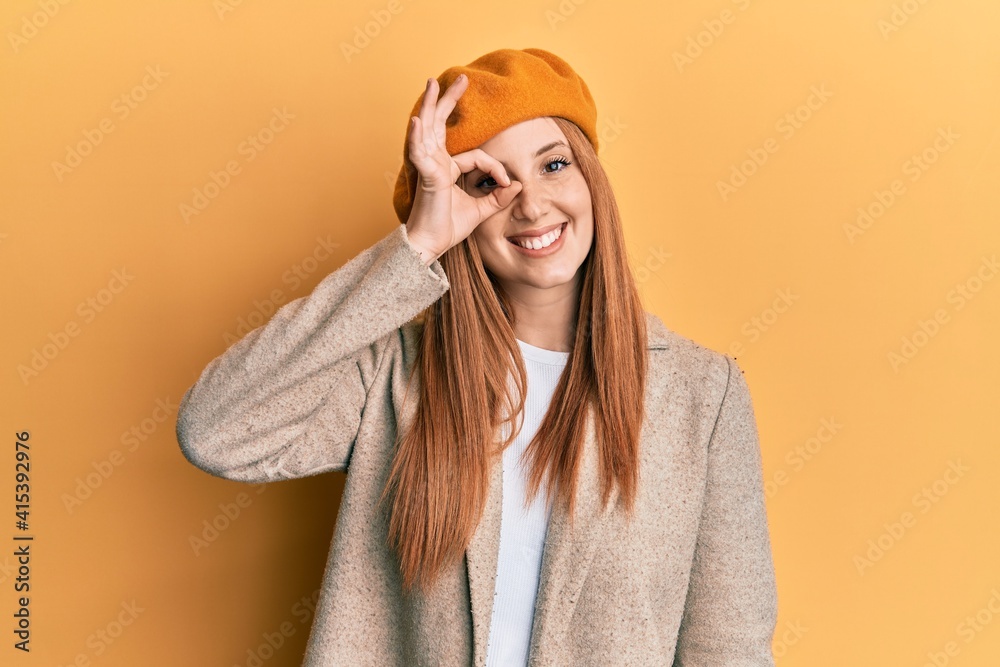 Young irish woman wearing french look with beret smiling happy doing ok sign with hand on eye looking through fingers