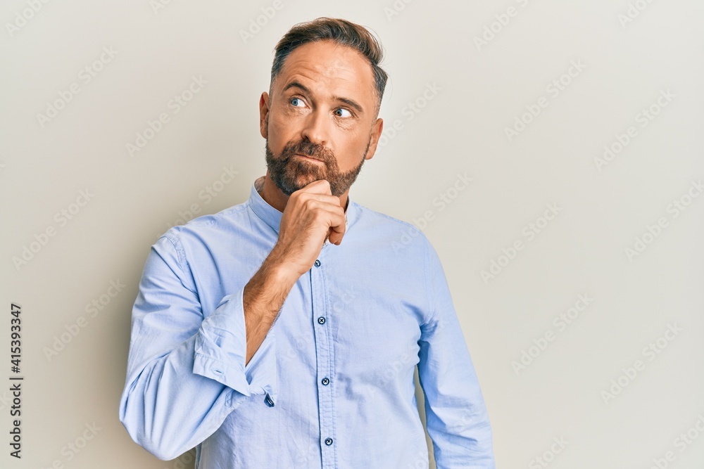 Handsome middle age man wearing business clothes thinking concentrated about doubt with finger on chin and looking up wondering Handsome middle age man wearing business clothes thinking concentrated about doubt with finger on chin and looking up wondering