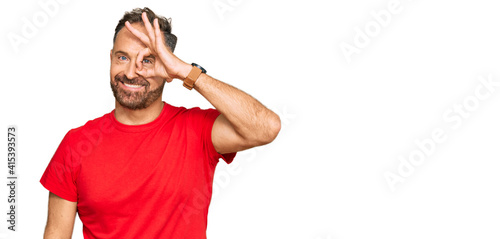 Handsome middle age man wearing casual red tshirt doing ok gesture with hand smiling, eye looking through fingers with happy face.
