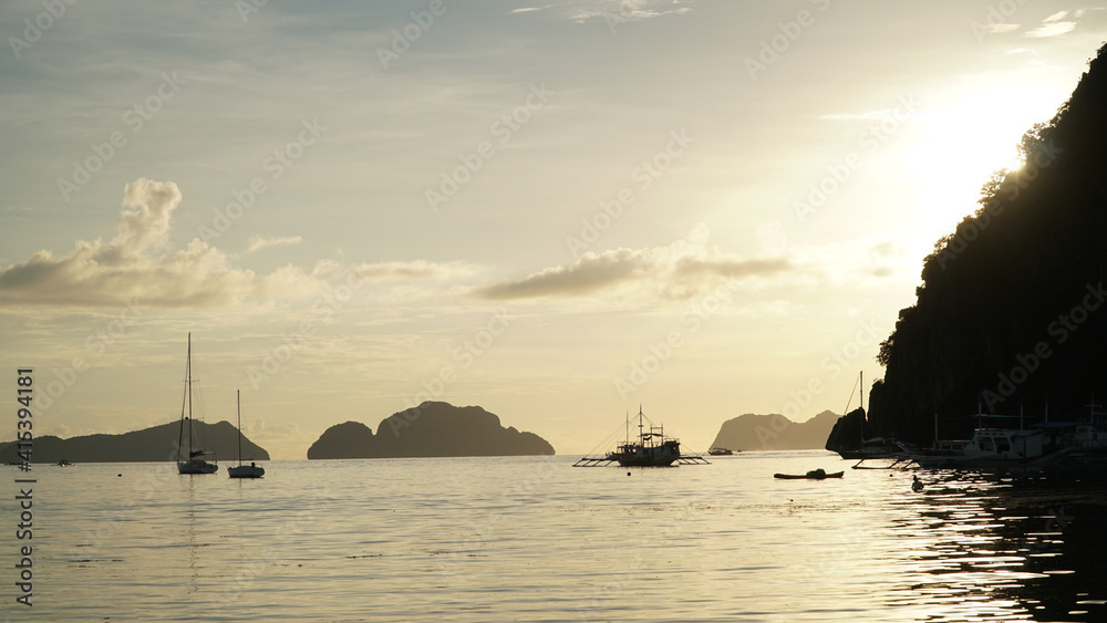 Sunset over the ocean with boats at El Nido Beach in Philippines.