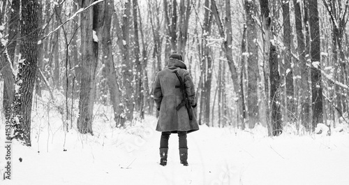 Soviet soldier in coat is standing with a gun in the winter forest 