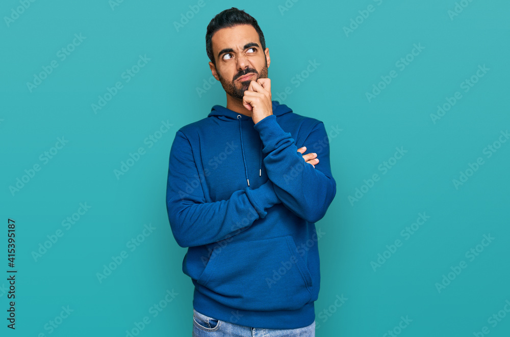 Young hispanic man wearing casual clothes serious face thinking about question with hand on chin, thoughtful about confusing idea