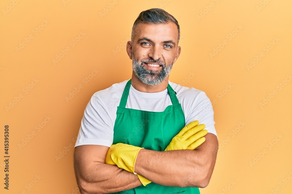 Middle age handsome man wearing cleaner apron and gloves happy face smiling with crossed arms looking at the camera. positive person. Middle age handsome man wearing cleaner apron and gloves happy face smiling with crossed arms looking at the camera. positive person.