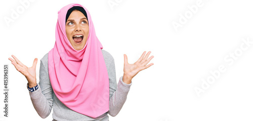 Young caucasian woman wearing traditional islamic hijab scarf crazy and mad shouting and yelling with aggressive expression and arms raised. frustration concept.