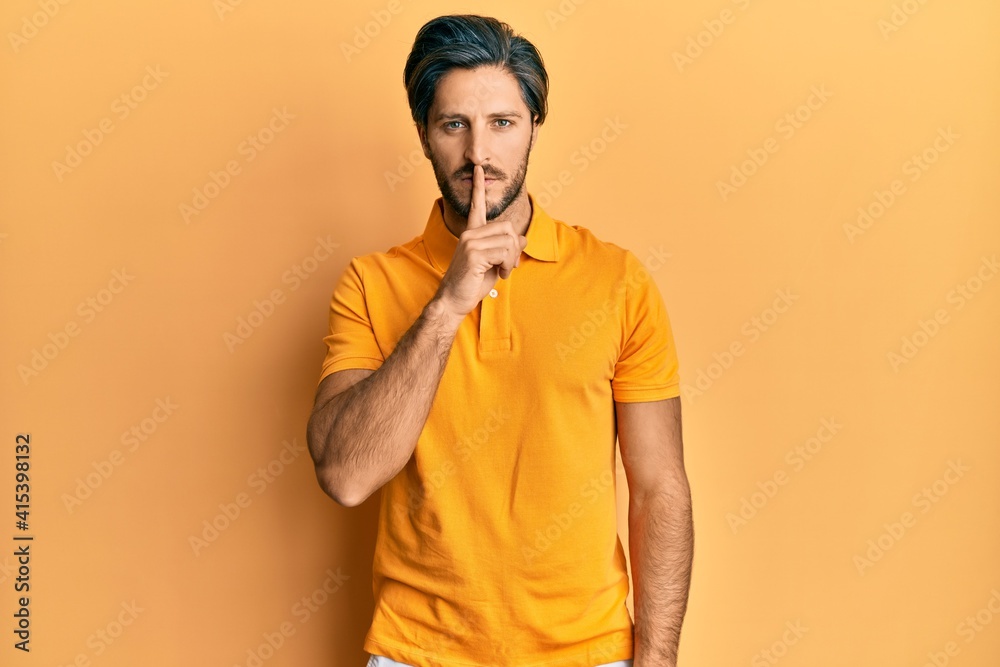 Young hispanic man wearing casual yellow t shirt asking to be quiet with finger on lips. silence and secret concept. Young hispanic man wearing casual yellow t shirt asking to be quiet with finger on lips. silence and secret concept.