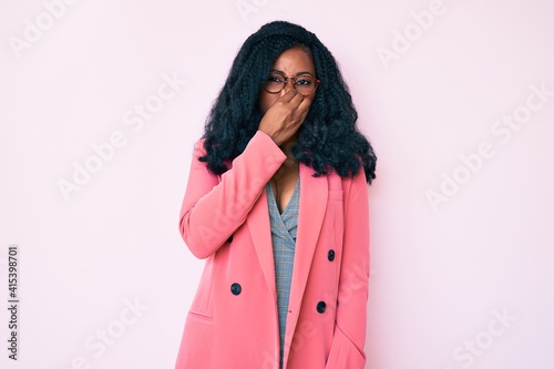 Beautiful african woman wearing business jacket and glasses smelling something stinky and disgusting, intolerable smell, holding breath with fingers on nose. bad smell © Krakenimages.com