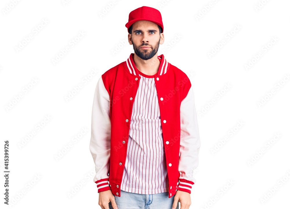 Young handsome man with beard wearing baseball jacket and cap with serious expression on face. simple and natural looking at the camera. Young handsome man with beard wearing baseball jacket and cap with serious expression on face. simple and natural looking at the camera.