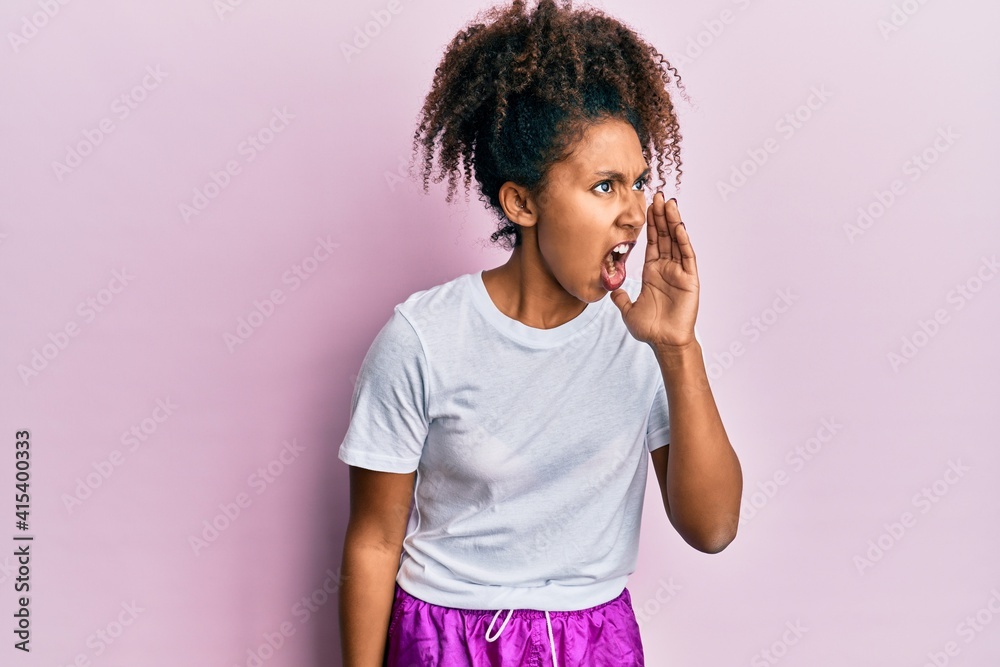 Beautiful african american woman with afro hair wearing sportswear shouting and screaming loud to side with hand on mouth. communication concept. Beautiful african american woman with afro hair wearing sportswear shouting and screaming loud to side with hand on mouth. communication concept.