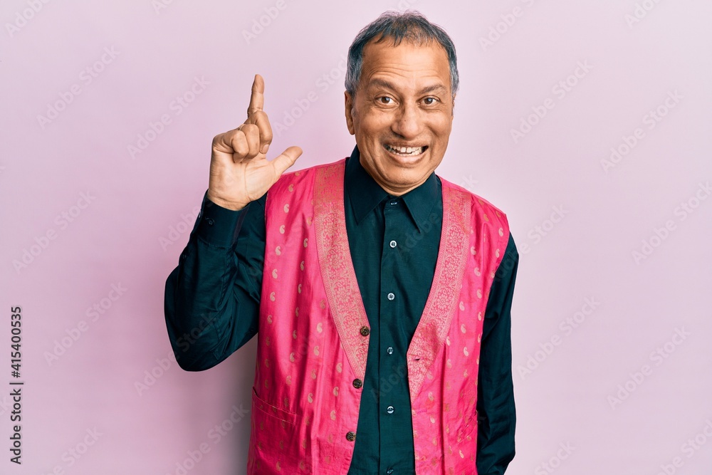 Middle age indian man wearing traditional indian clothes pointing finger up with successful idea. exited and happy. number one. Middle age indian man wearing traditional indian clothes pointing finger up with successful idea. exited and happy. number one.