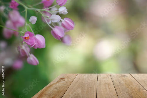 Wooden table with blur green leave and pink flower background.perspective view for display products.