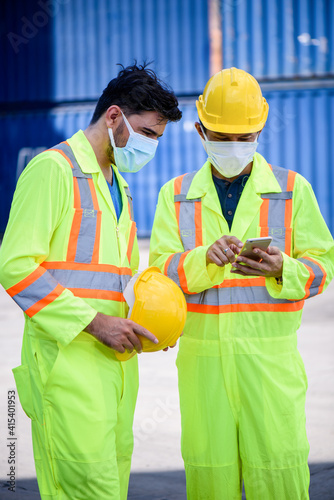 Engineer men wearing yellow hardhat standing near forklift cargo at the container yard and check for control loading Containers box from Cargo freight ship for import and export. Teamwork concept