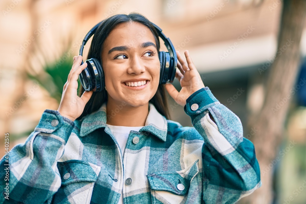 Young latin girl smiling happy using headphones at the city. Young latin girl smiling happy using headphones at the city.