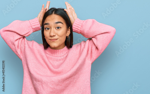 Young asian woman wearing casual winter sweater doing bunny ears gesture with hands palms looking cynical and skeptical. easter rabbit concept. photo