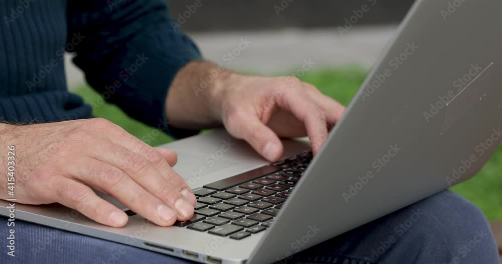Close up of male hands typing on modern laptop while sitting outdoors. Busy male in casual clothing working remotely on fresh air. Close up of male hands typing on modern laptop while sitting outdoors. Busy male in casual clothing working remotely on fresh air.