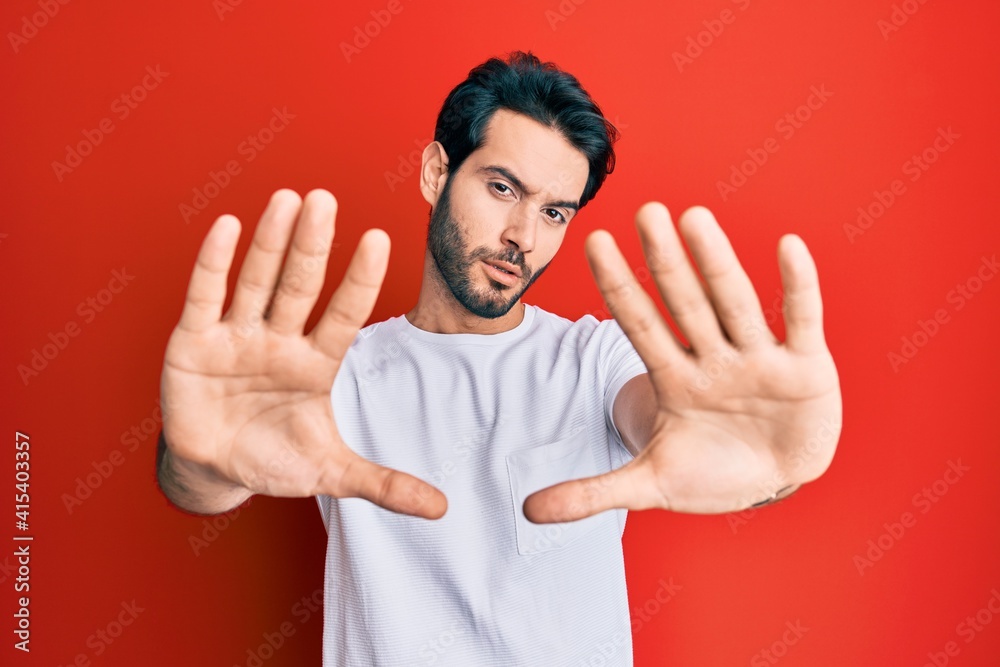 Young hispanic man wearing casual white tshirt doing frame using hands palms and fingers, camera perspective Young hispanic man wearing casual white tshirt doing frame using hands palms and fingers, camera perspective