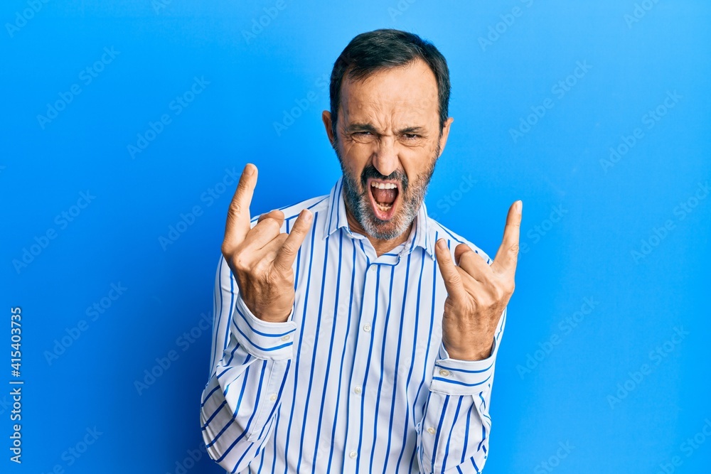 Middle age hispanic man wearing casual clothes shouting with crazy expression doing rock symbol with hands up. music star. heavy concept.