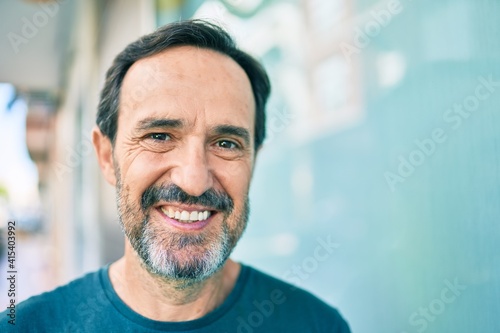 Middle age man with beard smiling happy outdoors leaning on the wall