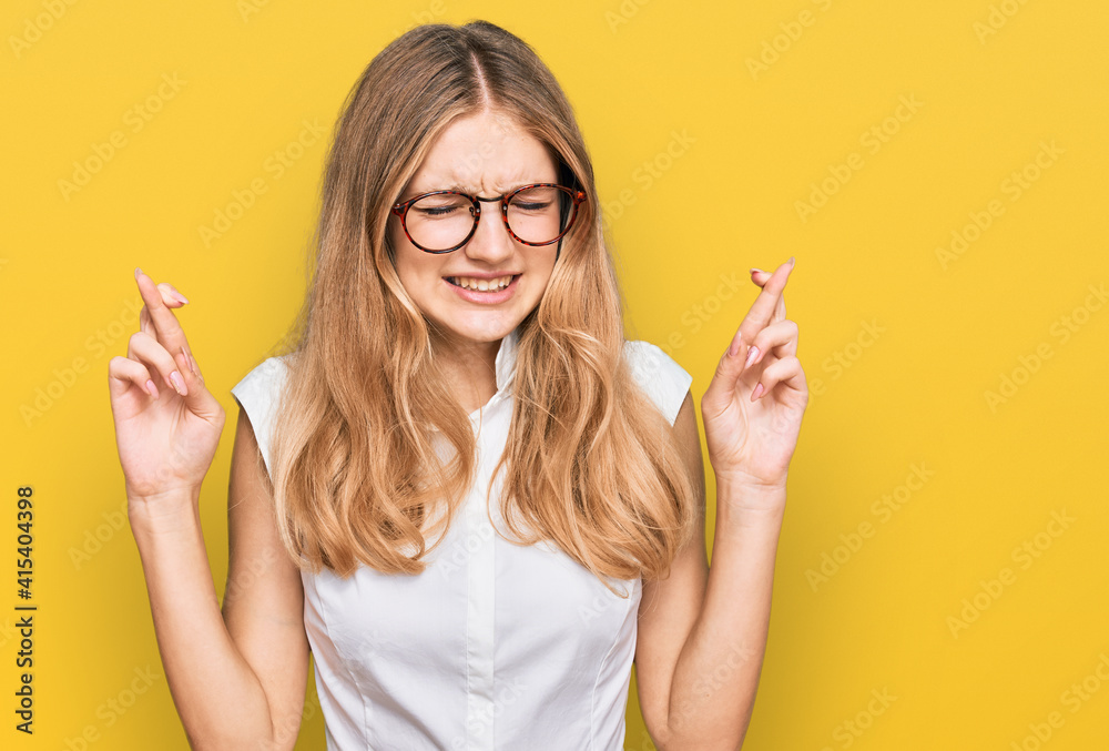 Beautiful young caucasian girl wearing casual clothes and glasses gesturing finger crossed smiling with hope and eyes closed. luck and superstitious concept.