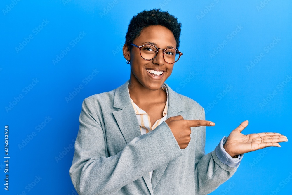 Young african american girl wearing business jacket and glasses amazed and smiling to the camera while presenting with hand and pointing with finger.
