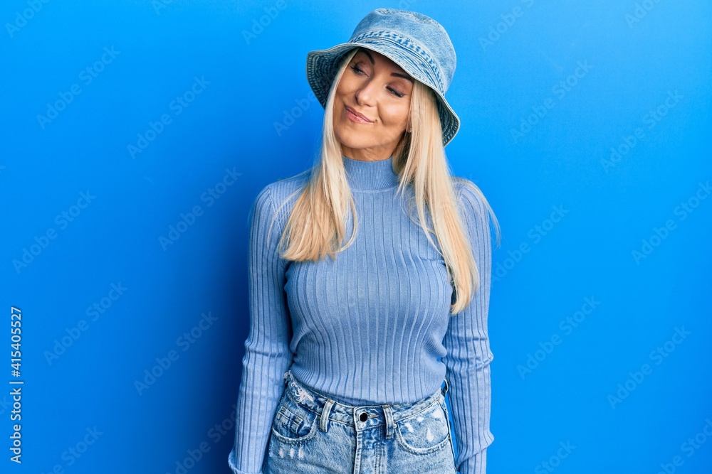 Young blonde woman wearing casual denim hat smiling looking to the side and staring away thinking. Young blonde woman wearing casual denim hat smiling looking to the side and staring away thinking.