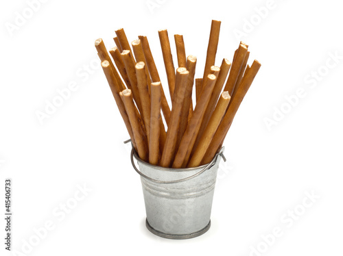 Sweet straws in a metal bucket. Dry baked goods in the form of thin sticks. White background.