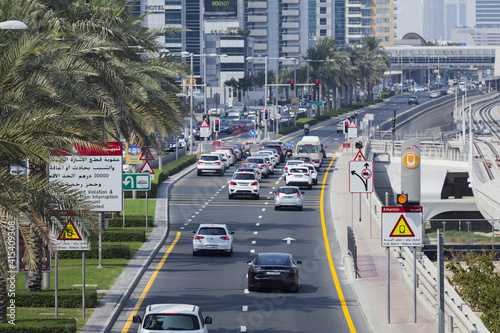 Traffic at Sheikh Zayed Road in Dubai, UAE. Cars are slowing down for the red light. Lots of traffic signs around. Vehicles waiting for the green light next to the metro station. Developed transport.