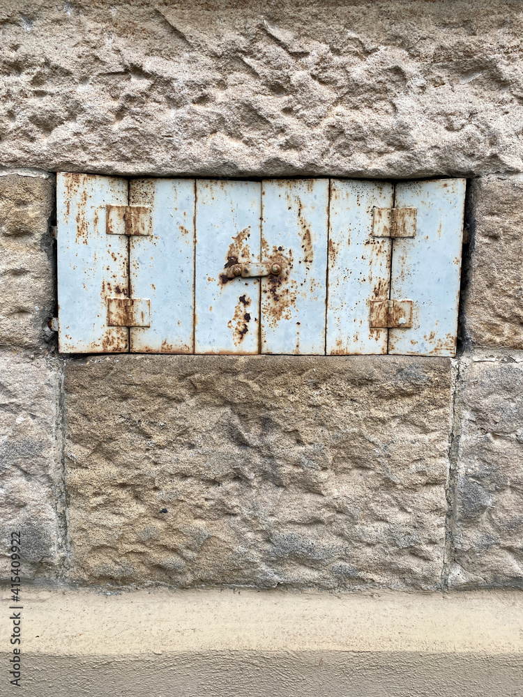 Verschlossene Fensterluke in rauer Natursteinwand., Laden aus dünnen verrsosteten Blech Verschlossene Fensterluke in rauer Natursteinwand., Laden aus dünnen verrsosteten Blech