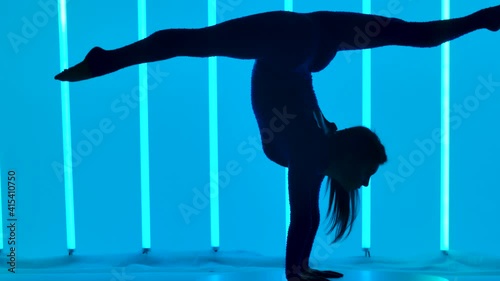 Silhouette of a woman gymnast doing a handstandin the studio against the background of multicolored neon tubes. The movement of the camera from the girl's hands to her legs. Slow motion. Close up.