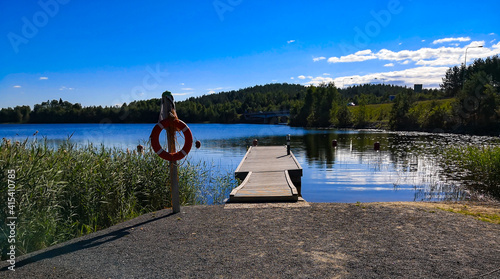 Sunny lake view with wooden pier and life belt.