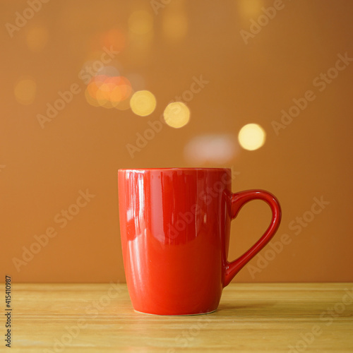 Red coffee cup on wooden desk on brown background with bokeh