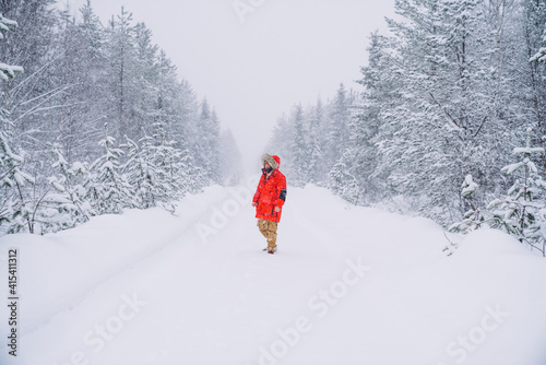 Male in winter trendy bright red coat feeling warm recreating on wanderlust destination on north, man walking on snowy frosty road in wood with tall frozen trees