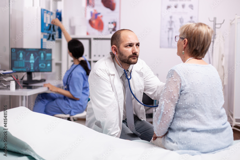 Healthcare specialist using stethoscope in private clinic using stethoscope. Medical practitioner examining lungs of caucasian in modern clinic dressed in white coat.