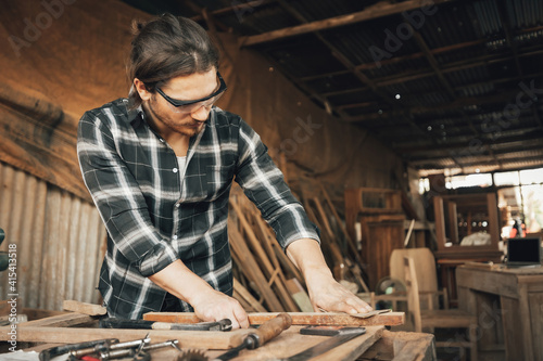 male carpenter using sandpaper on a piece of wood in workshop(vintage tone)