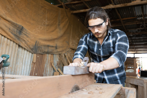 male carpenter holding a plane, planing and shaving a piece of wood in a clamp