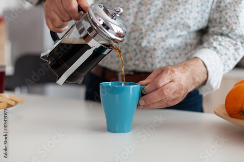 Close up of elderly man hands pouring coffee in cup during breakfast sitting in modern kitchen. Elderly person in the morning enjoying fresh brown espresso from vintage mug, filter relax refreshment