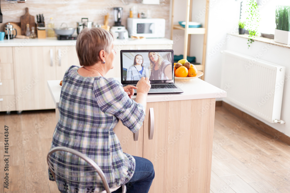 Happy senior woman during a video conference with family using laptop in kitchen. Online call with daughter and niece. Old elderly person using modern communication online internet web techonolgy. Happy senior woman during a video conference with family using laptop in kitchen. Online call with daughter and niece. Old elderly person using modern communication online internet web techonolgy.
